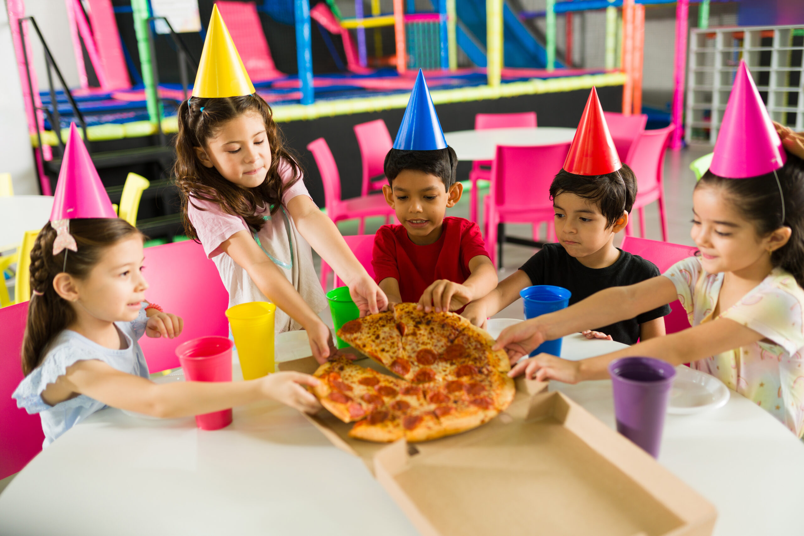 Happy group of kids eating delicious pizza while celebrating a birthday party and having fun together in the playroom